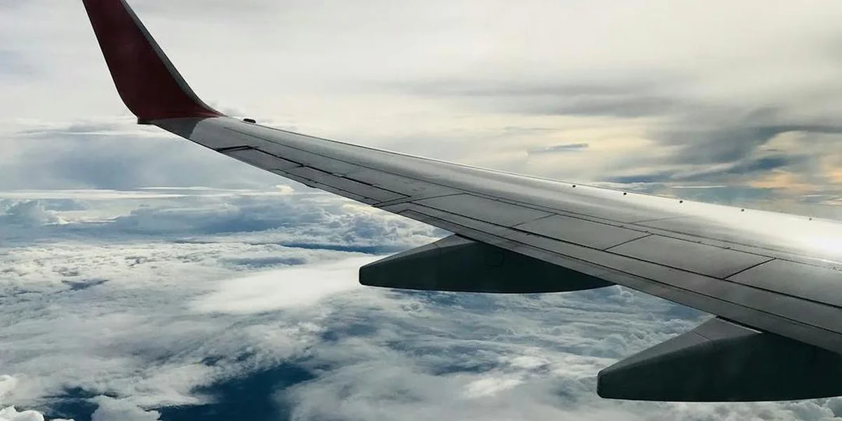 Airplane wing viewed from a window above the clouds, symbolizing travel and inner journey.