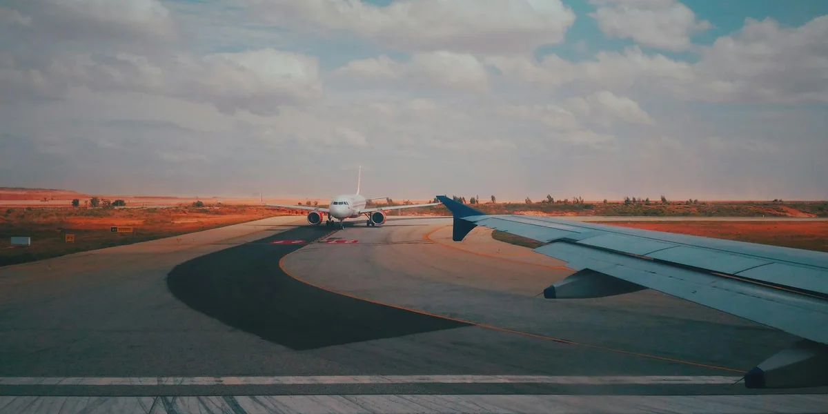 Airplane wing on a runway with a distant terminal under a cloudy blue sky