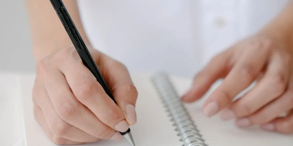 Close-up of hands writing in a notebook with a pen, symbolizing recording dreams and their emotional meanings.