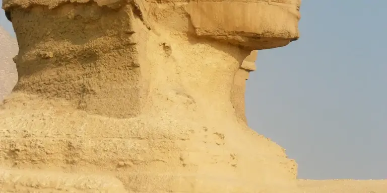 Close-up of a weathered sandstone statue head from ancient Egypt against a clear blue sky.