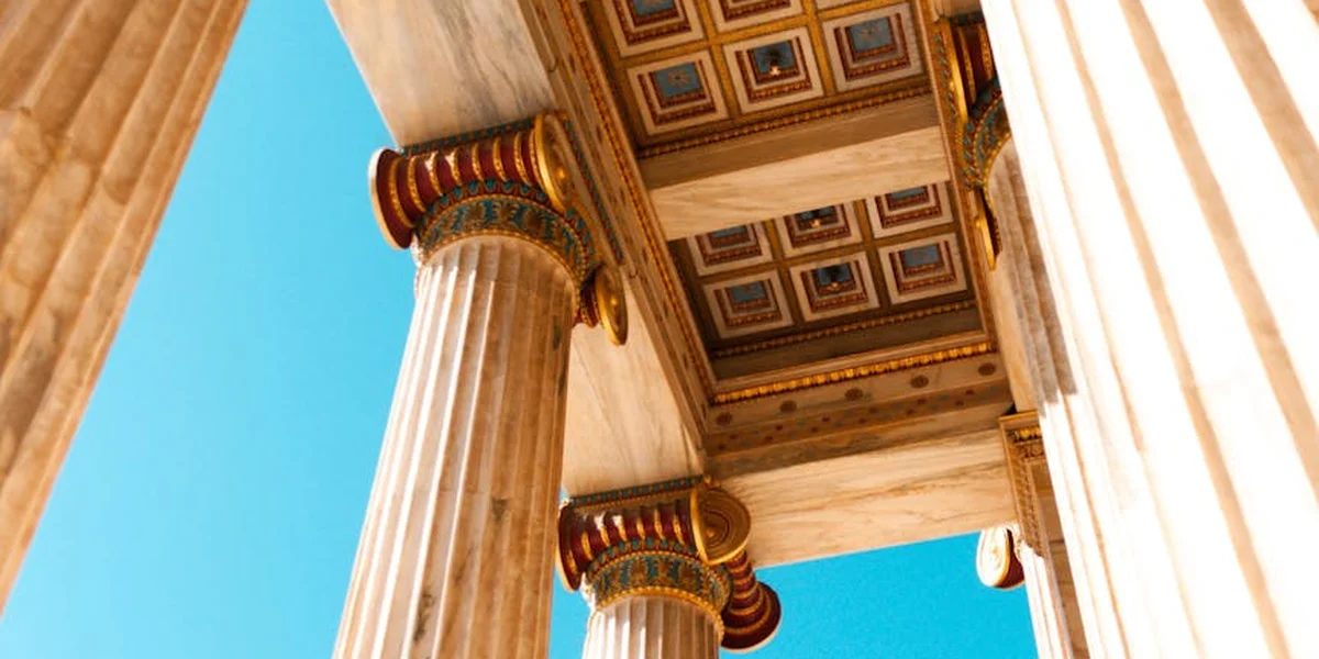 Rows of ancient Greek temple columns with ornate capitals set against a clear blue sky.