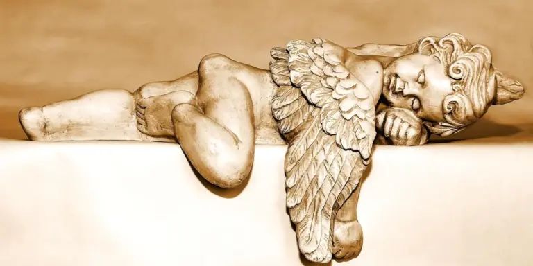 A stone angel statue lying down with folded wings resting on a ledge