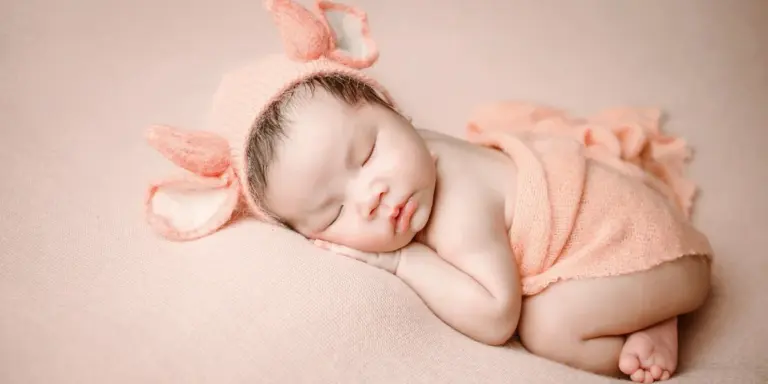 Sleeping baby wearing a peach knit wrap and bunny-ear headband
