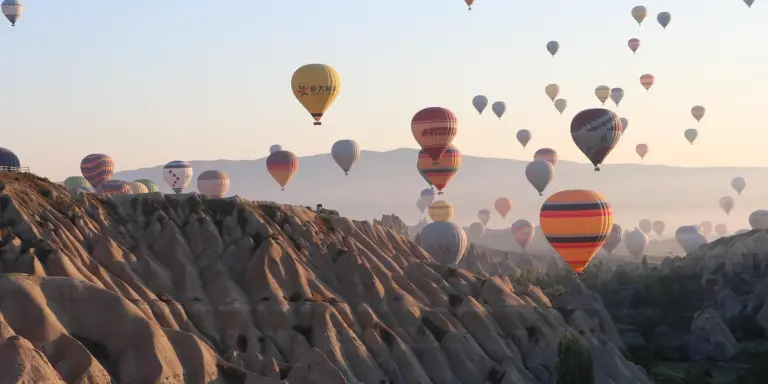 Colorful hot air balloons floating over a rocky valley at dawn.