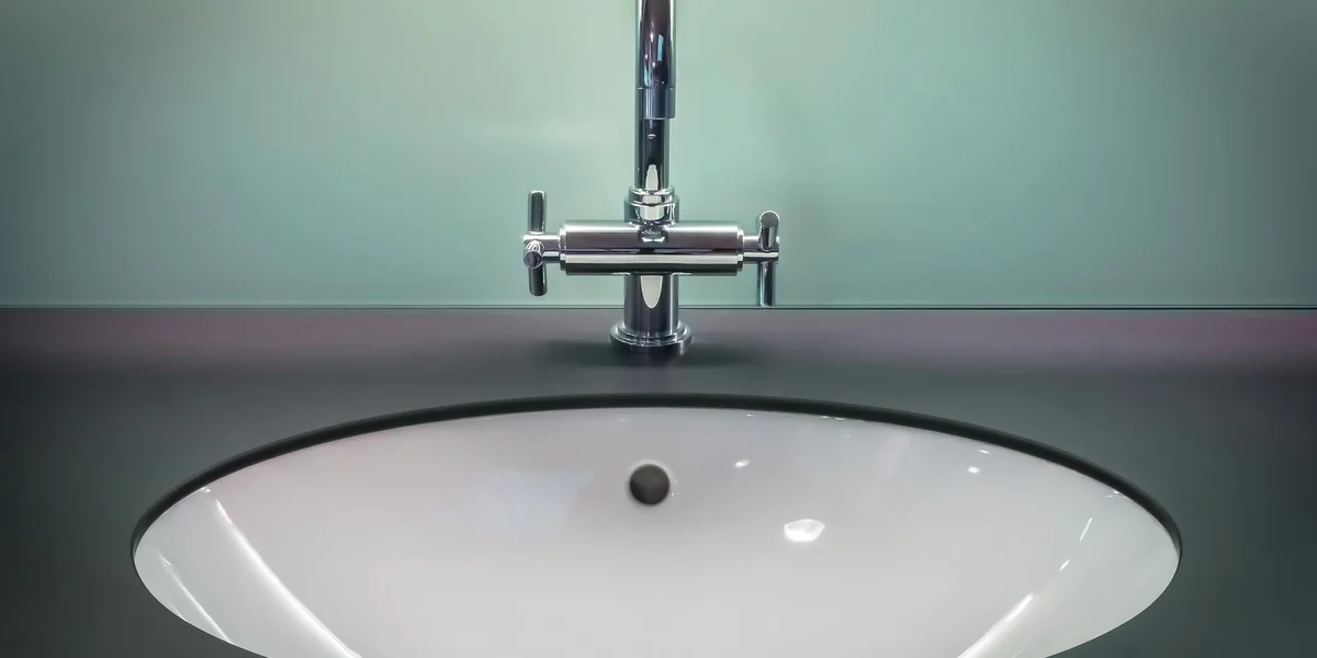 Close-up of a modern bathroom sink with a chrome faucet against a pale green wall.
