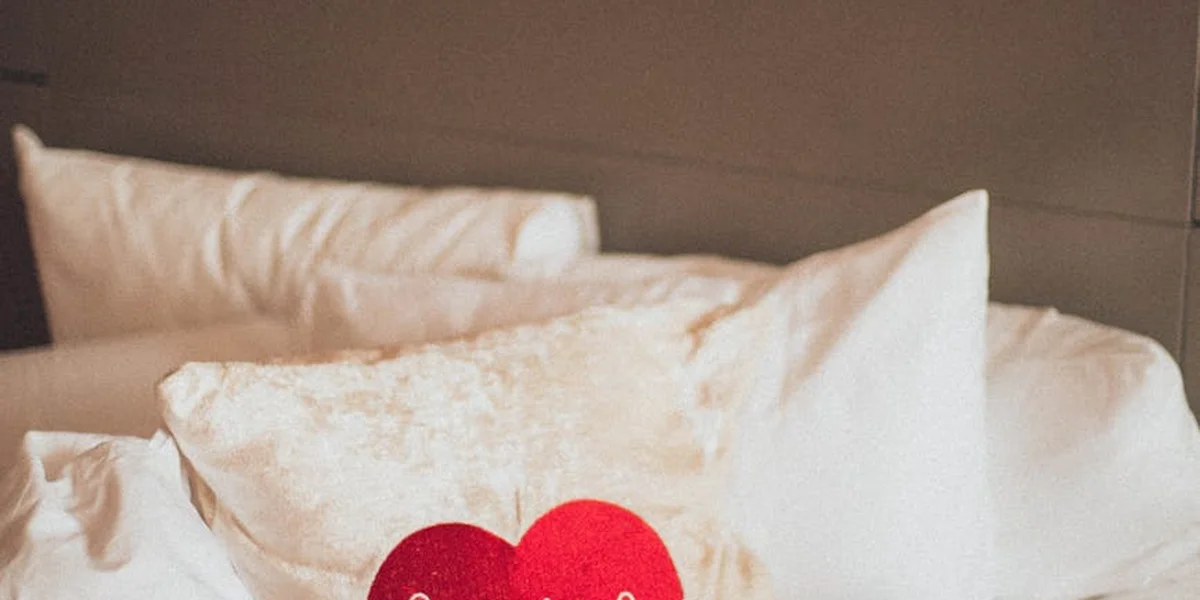 A cozy bed with white pillows and two red heart-shaped cushions, suggesting intimacy and dream imagery.