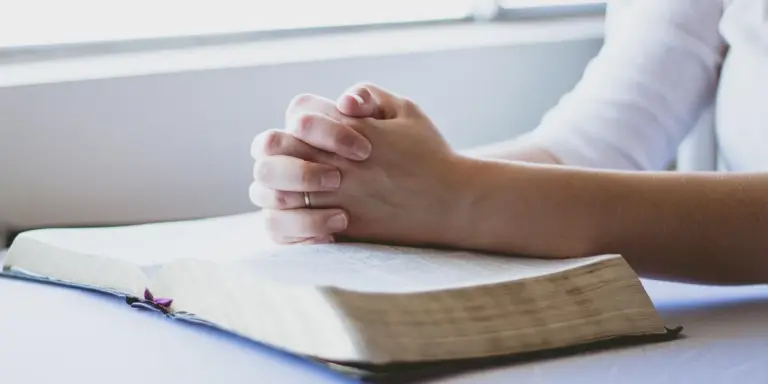 Clasped hands resting on an open Bible, symbolizing prayer and study as part of interpreting body parts in dreams.
