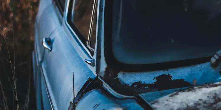 Close-up of a blue car with front-end damage and a cracked windshield, parked outdoors.