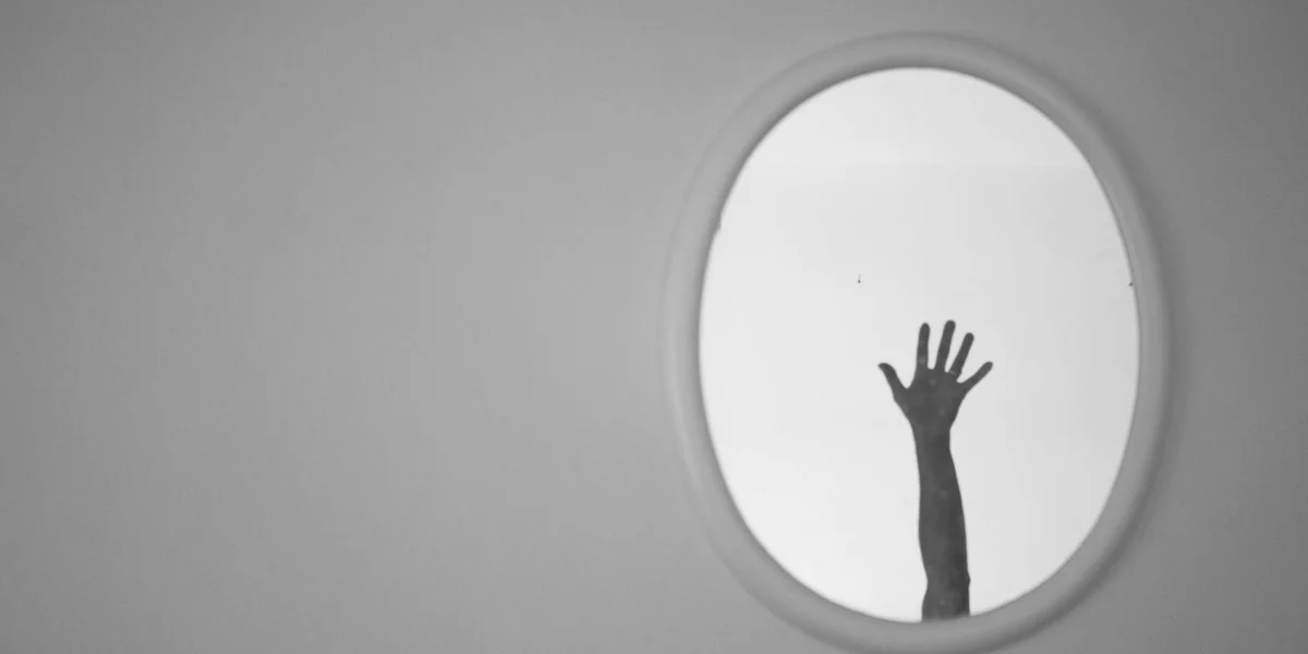Silhouette of an arm reaching upward through an oval window in a gray wall.