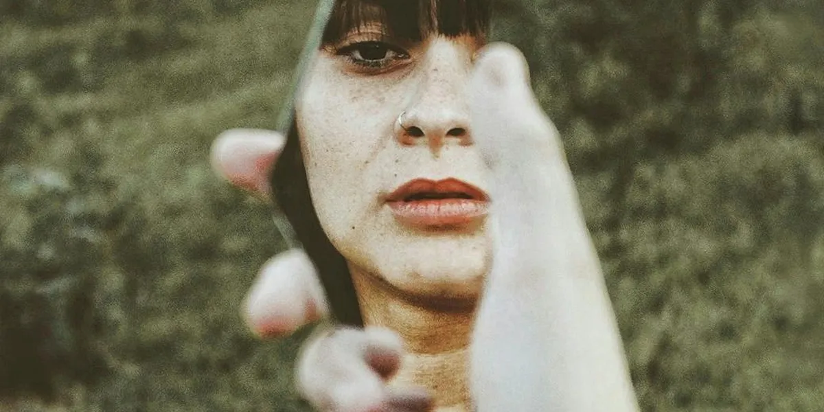 Close-up of a woman's face with one hand reaching toward the camera, a soft, blurred background.