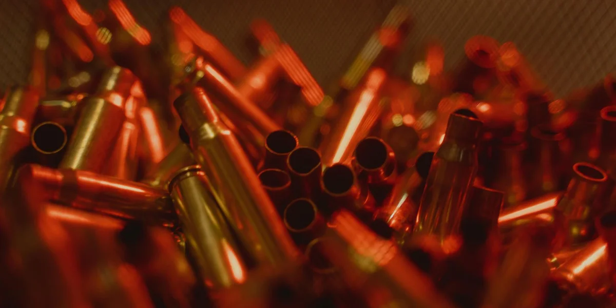 Close-up of red-tinged bullet casings scattered in a chaotic arrangement, suggesting tension and danger.