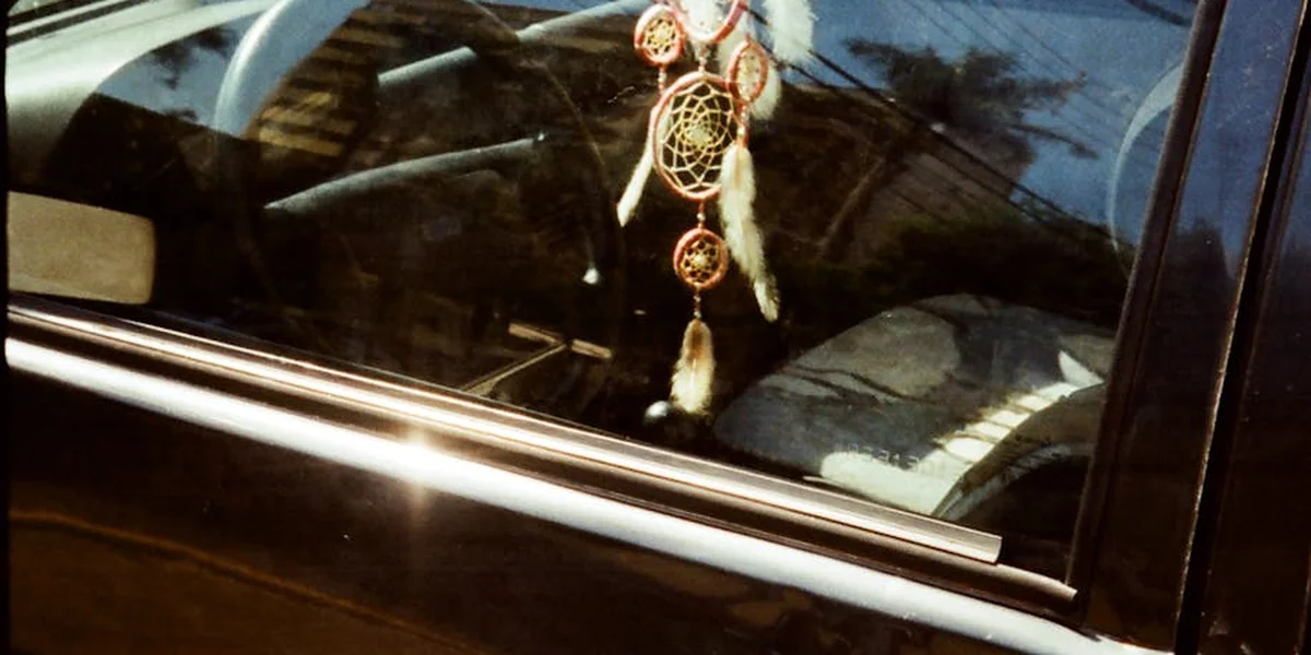 Dreamcatcher hanging from a car window with sunlight reflecting on the glass