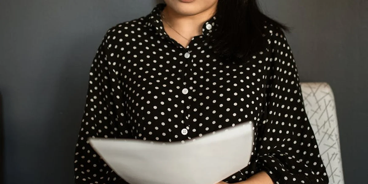 Person wearing a black polka-dot shirt sits at a desk, holding a sheet of paper and contemplating a career change.