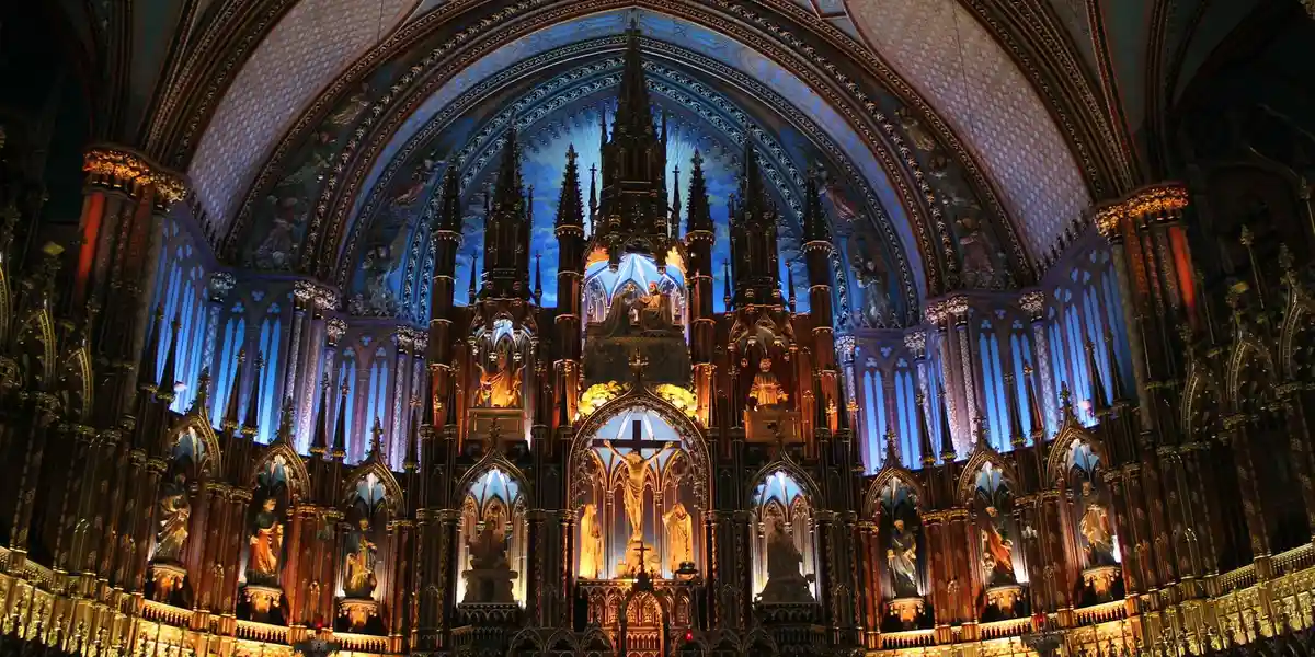 Interior of a grand cathedral with ornate gold altarpieces, arches, and blue lighting illuminating the sacred space.