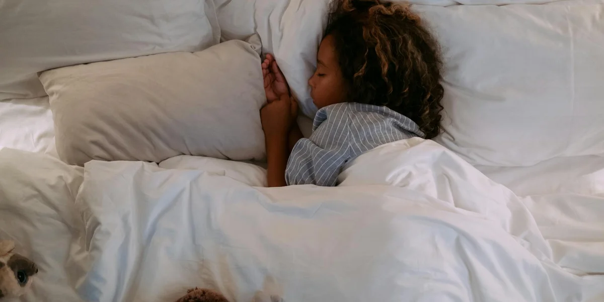 A young child sleeping peacefully on a white bed with a pillow.