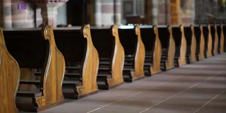 Rows of wooden church pews in a sanctuary, extending toward the altar.