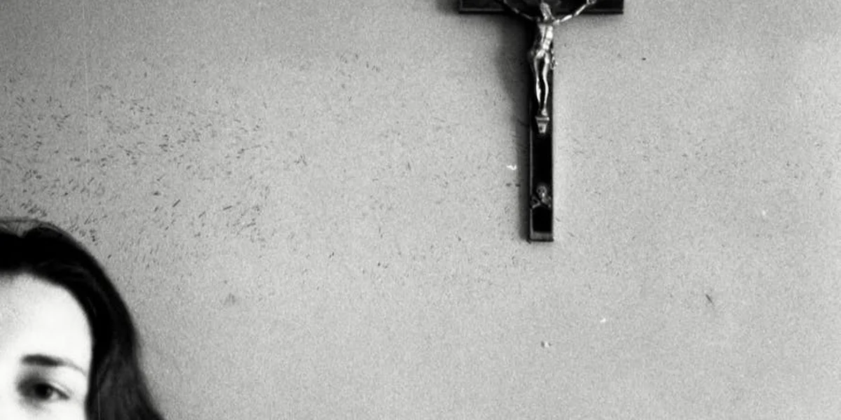 Partial view of a person at the edge of the frame with a crucifix on the wall of a church.
