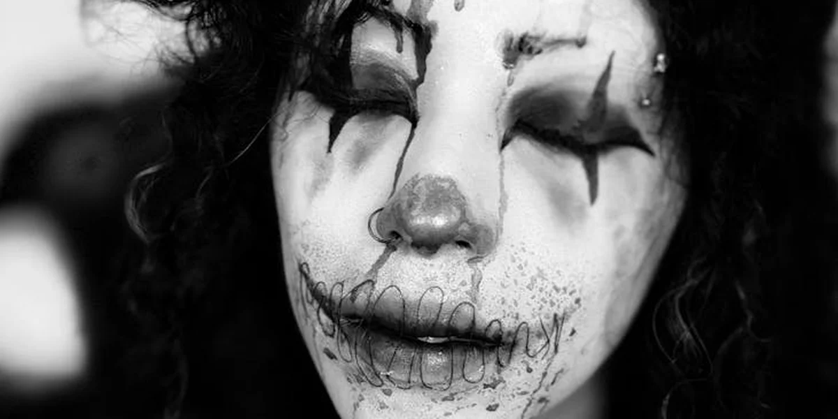 Black-and-white image of a clown with smeared makeup and closed eyes, conveying melancholy and emotional intensity.