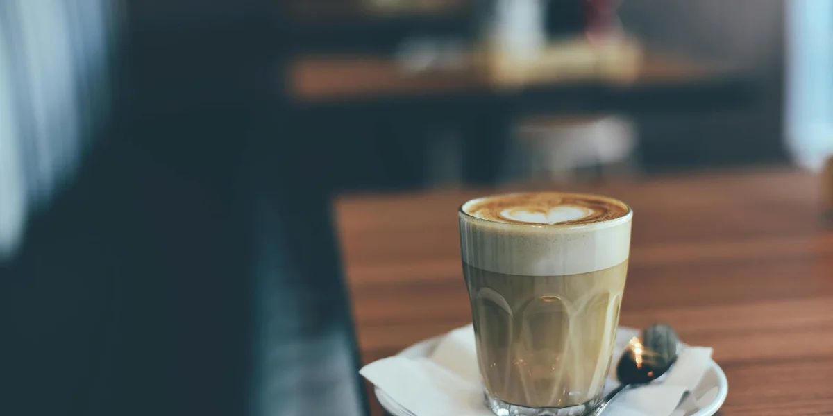 Latte with heart-shaped foam art on a wooden cafe table