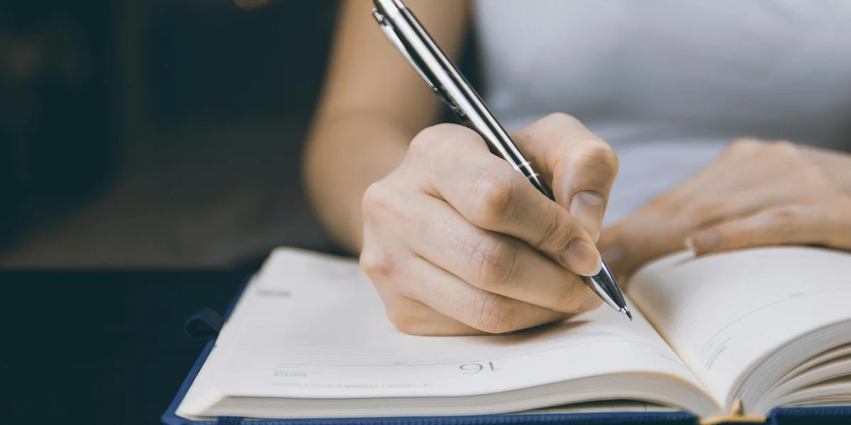 Close-up of a hand holding a pen and writing in an open notebook