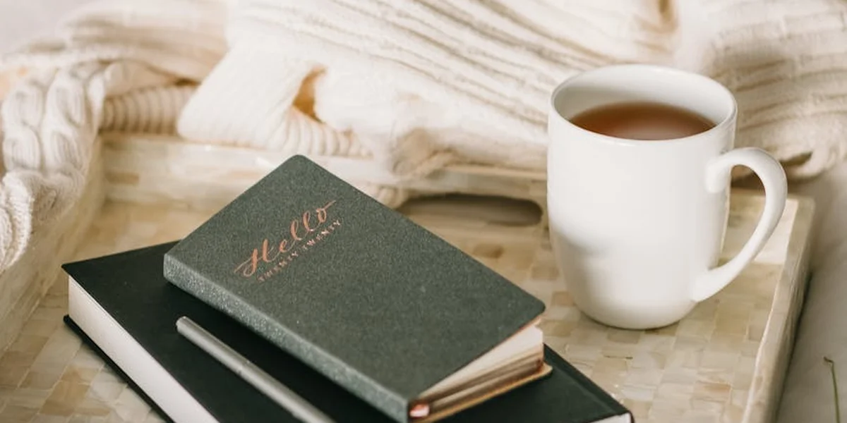 A green notebook on a bed with soft blankets and a white mug, creating a cozy study setup to explore lucid dreaming techniques.