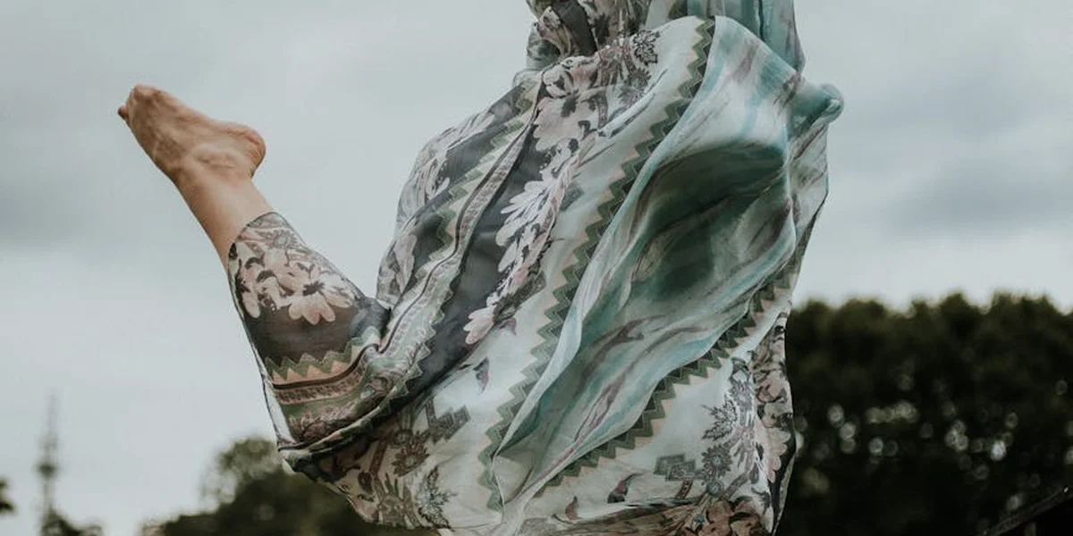 A dancer in flowing patterned fabric leaping or spinning outdoors, feet lifted and fabric fluttering