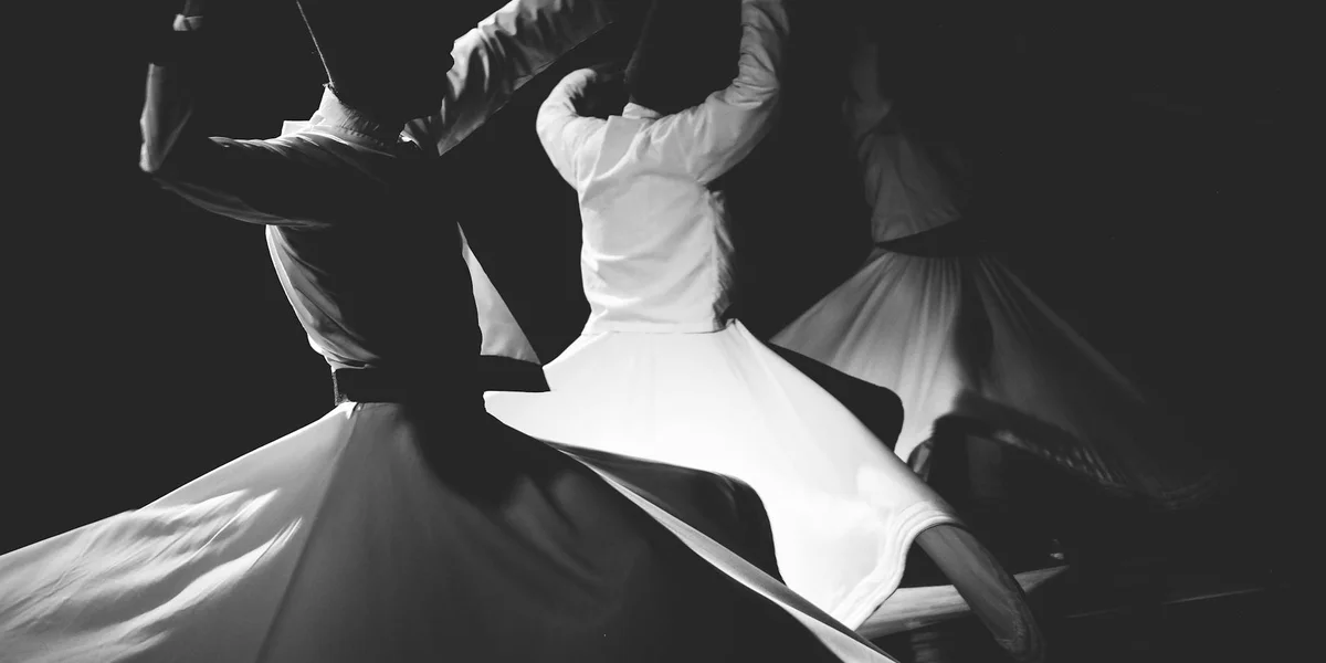 Black-and-white image of dancers twirling in a circle, with a central figure wearing a flowing white dress.