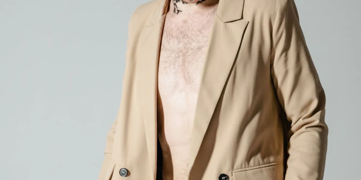 Partial view of a person wearing a beige blazer standing against a pale gray background.