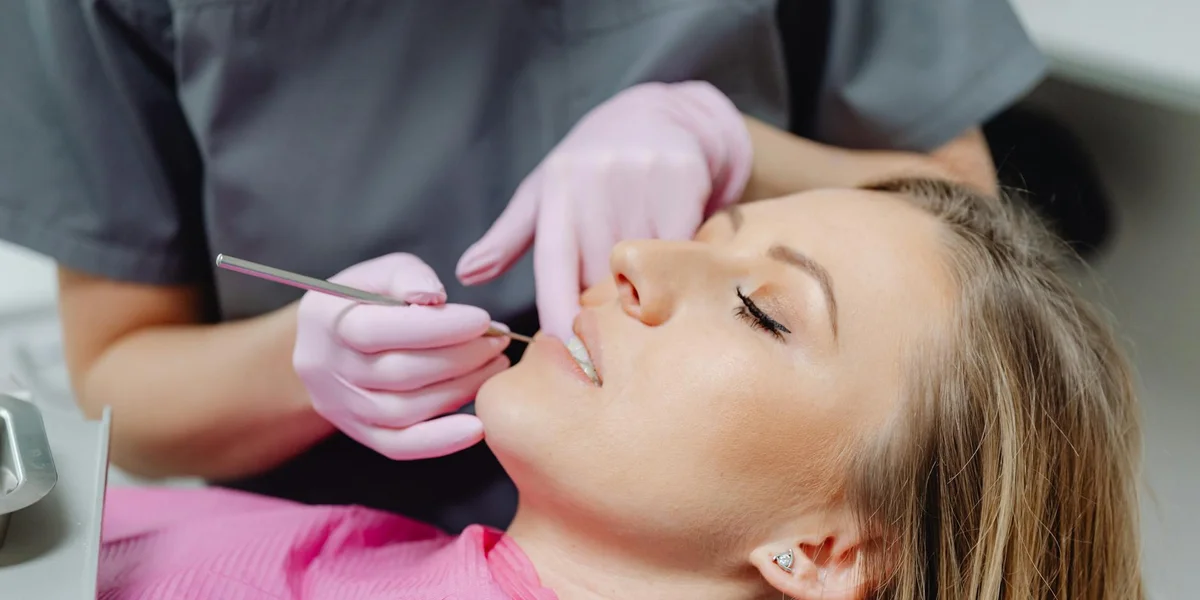 A patient reclining in a dental chair while a dentist wearing pink gloves uses a dental instrument near the mouth.