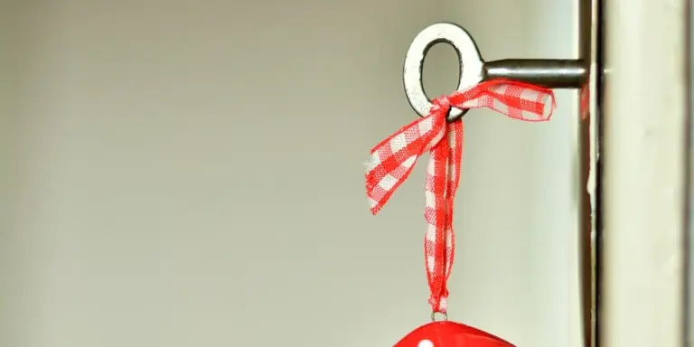 Close-up of a metal door handle with a red-and-white checkered ribbon tied around it and a key visible near the handle.