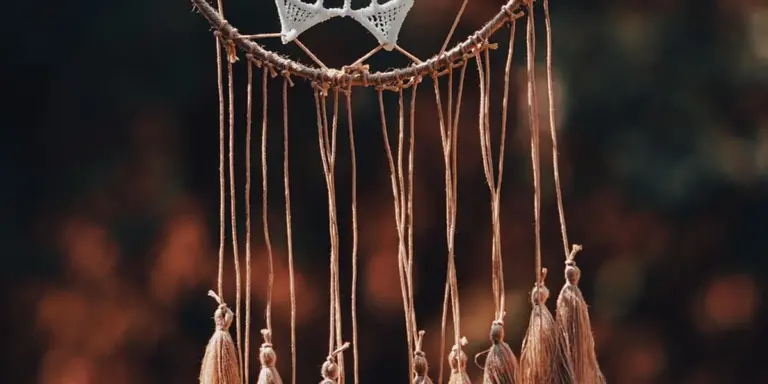Close-up of a dreamcatcher with hanging threads and beads against a blurred background