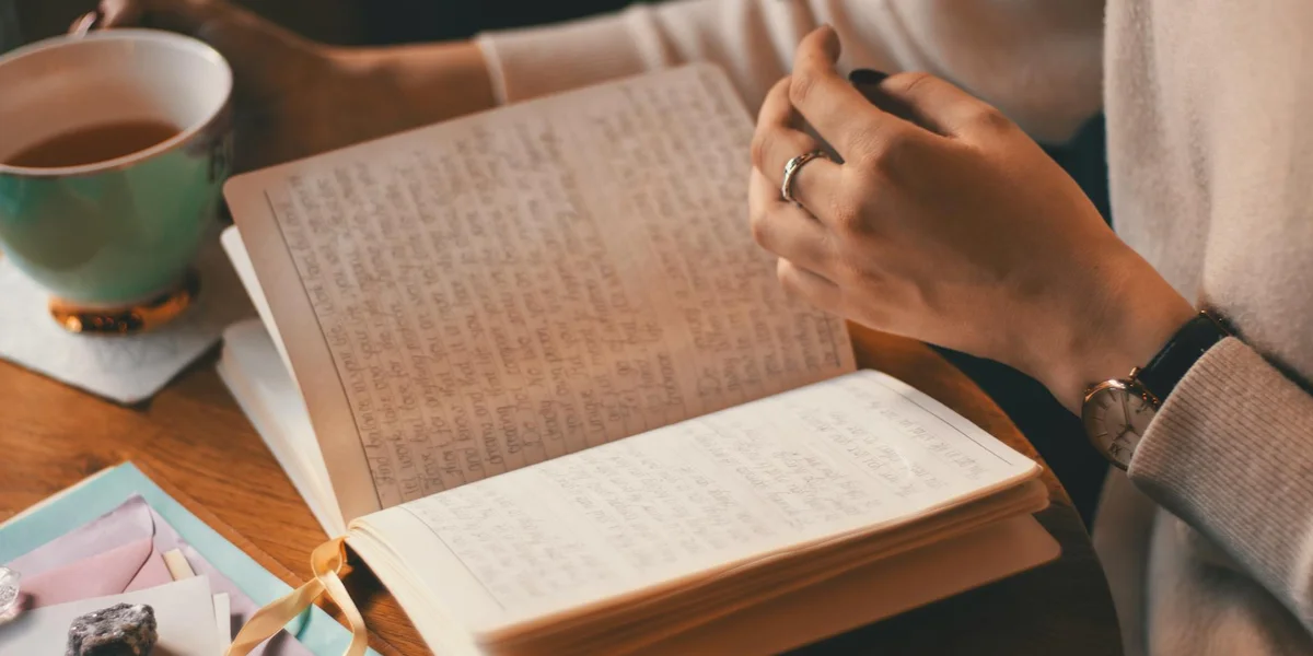 A person writes in a notebook at a wooden table with a cup of tea nearby, capturing a moment of reflection and dream analysis.
