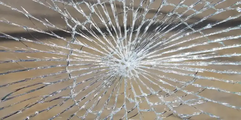 Close-up of a glass surface cracked in a spiderweb pattern with a central impact point.