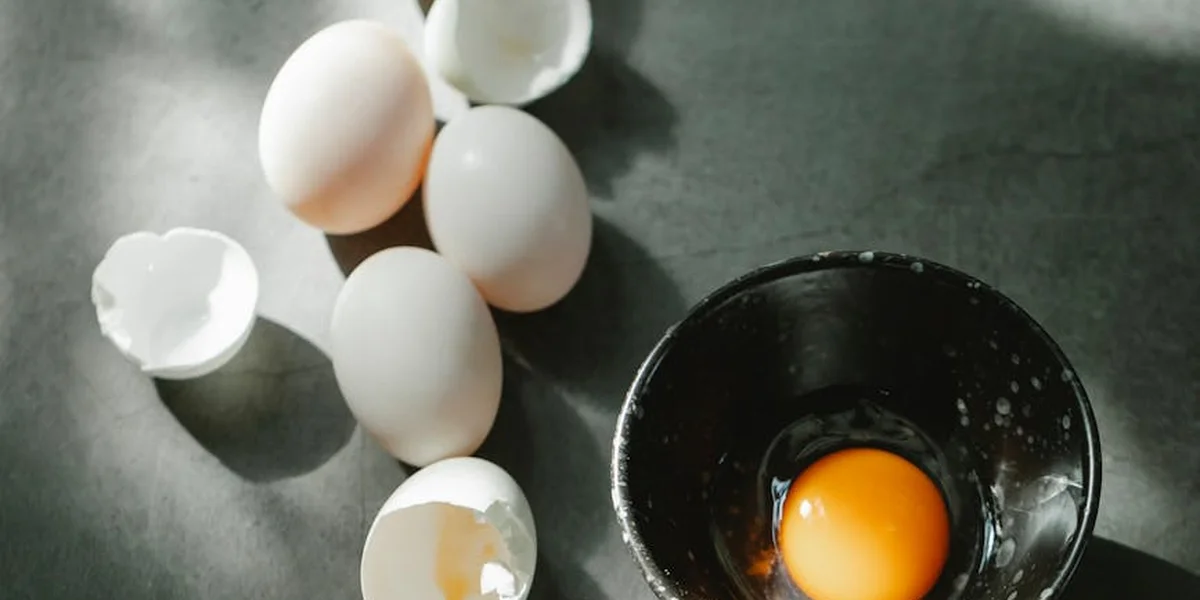 A still life of white eggs, broken shells, and a bright orange egg yolk in a dark bowl on a gray surface, symbolizing birth, nourishment, and potential in dreams.