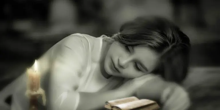 A person lying down with eyes closed beside a lit candle in a dim setting.