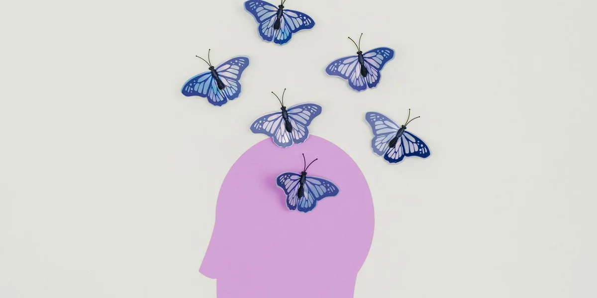 Profile silhouette of a head in lavender with blue butterflies hovering around it, representing dream imagery and interpretation.