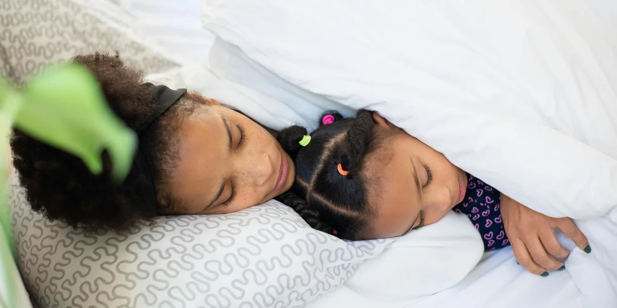 Two children sleeping peacefully under a white blanket, nestled close with calm expressions