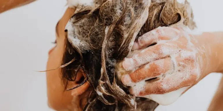 Close-up of a person’s hands massaging soap into wet hair, creating a lather.
