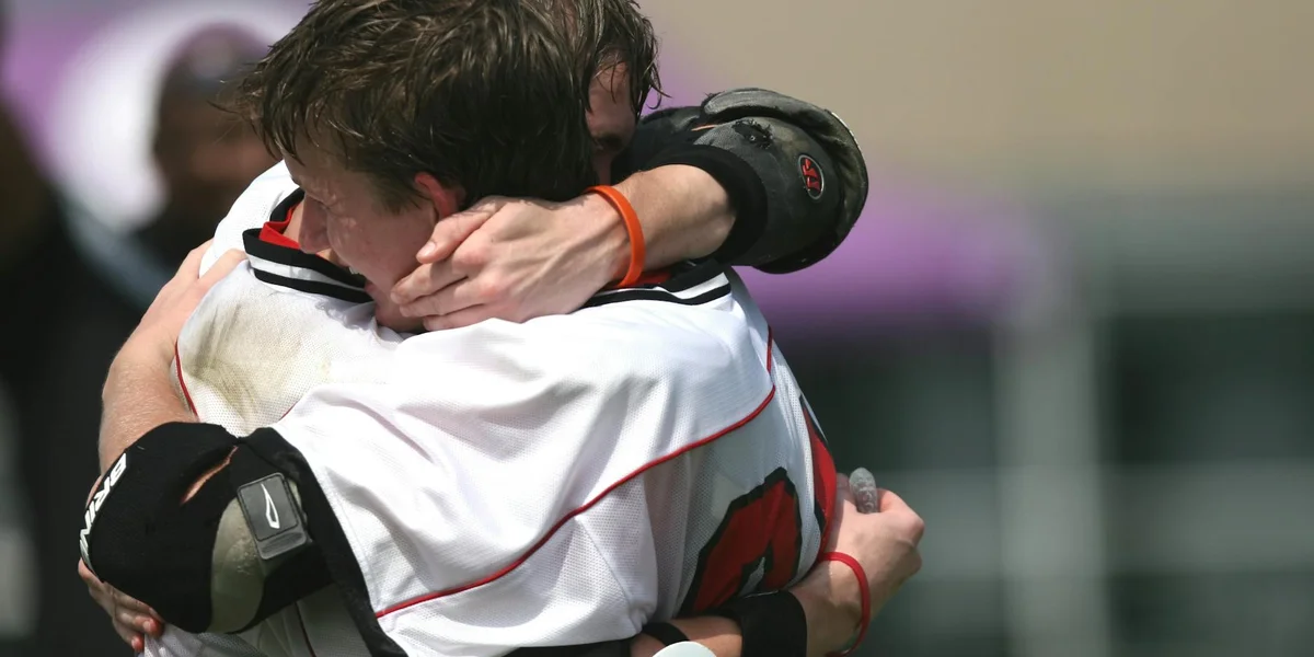 Two people sharing a close, comforting hug on a sports field, arms wrapped around each other.