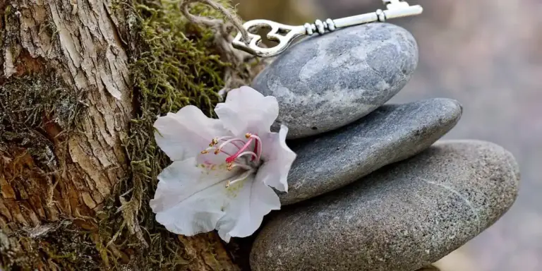 Antique key resting on a stack of smooth stones beside a white flower, symbolizing unlocking inner potential