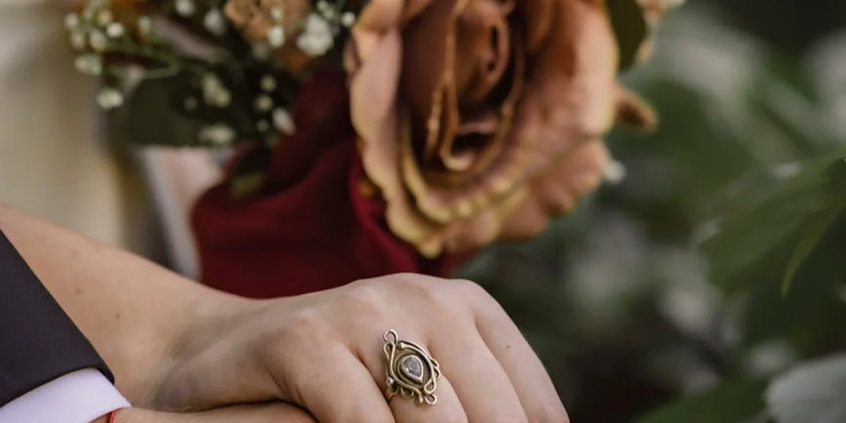 Close-up of a hand wearing an ornate ring, with a soft floral background.