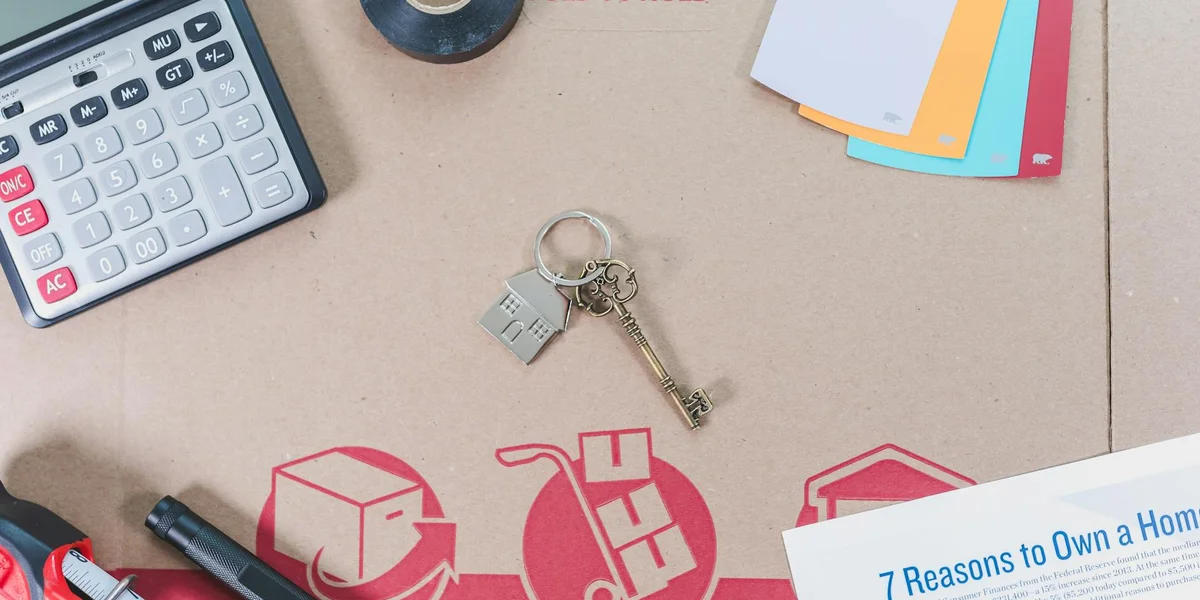 A desk with a keyring featuring multiple keys and a small padlock charm, along with a calculator and colorful file folders on a light brown surface.