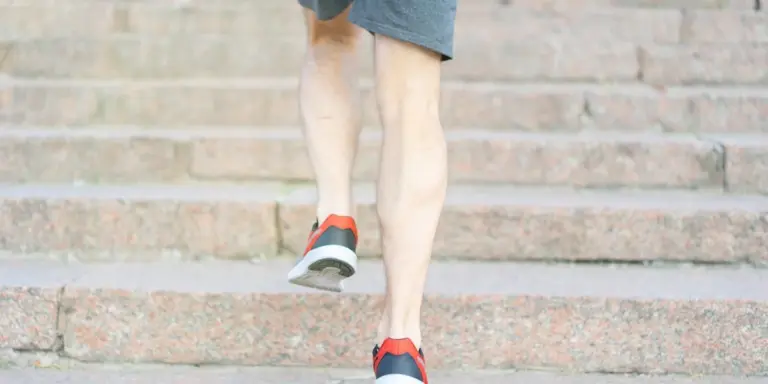 Close-up of a person’s legs running up outdoor stone steps, wearing red and black sneakers.