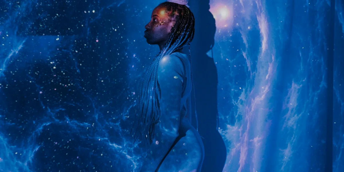 A silhouette of a person with braided hair standing sideways against a vast blue cosmic backdrop, representing dreaming, symbolism, and spiritual awakening.