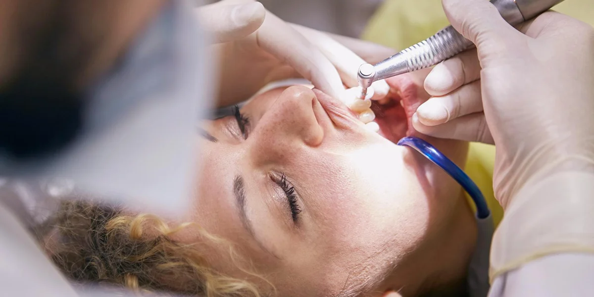 Close-up of a patient in a dental chair receiving treatment, with dental tools near the mouth.