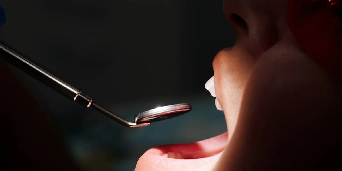 Close-up of a dentist's mirror hovering over an open mouth, showing teeth during a dental checkup.
