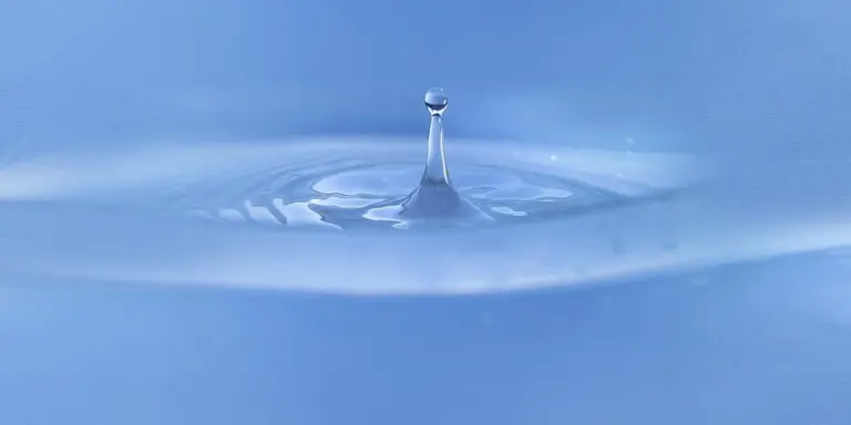 Close-up of a single water droplet creating ripples on a blue water surface