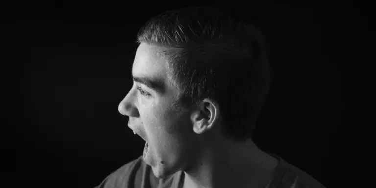 Black-and-white portrait of a young man with mouth wide open as if shouting, against a dark background.