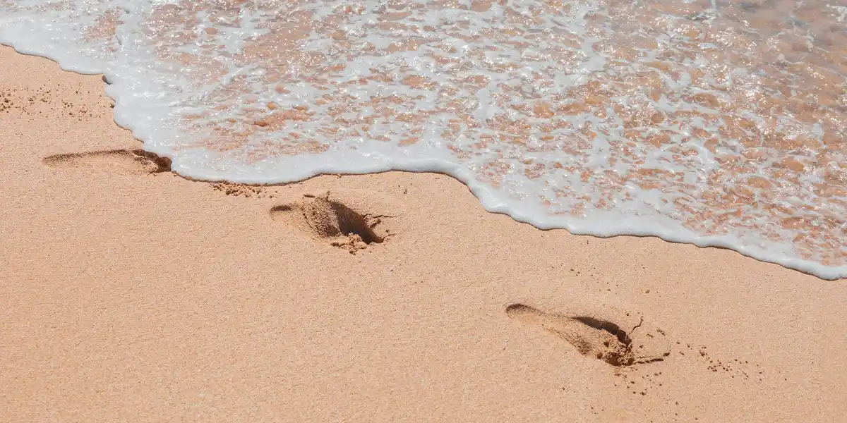 Footprints in wet sand along a beach with waves washing over them.