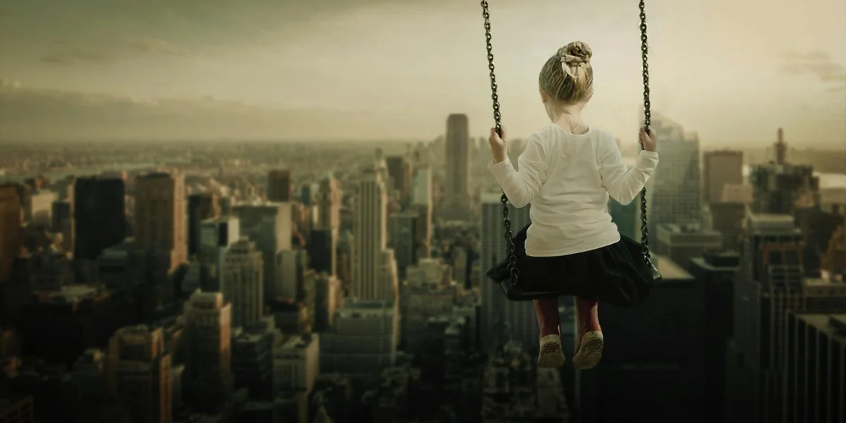 A young child on a swing high above a dense city skyline, looking out over the urban landscape.